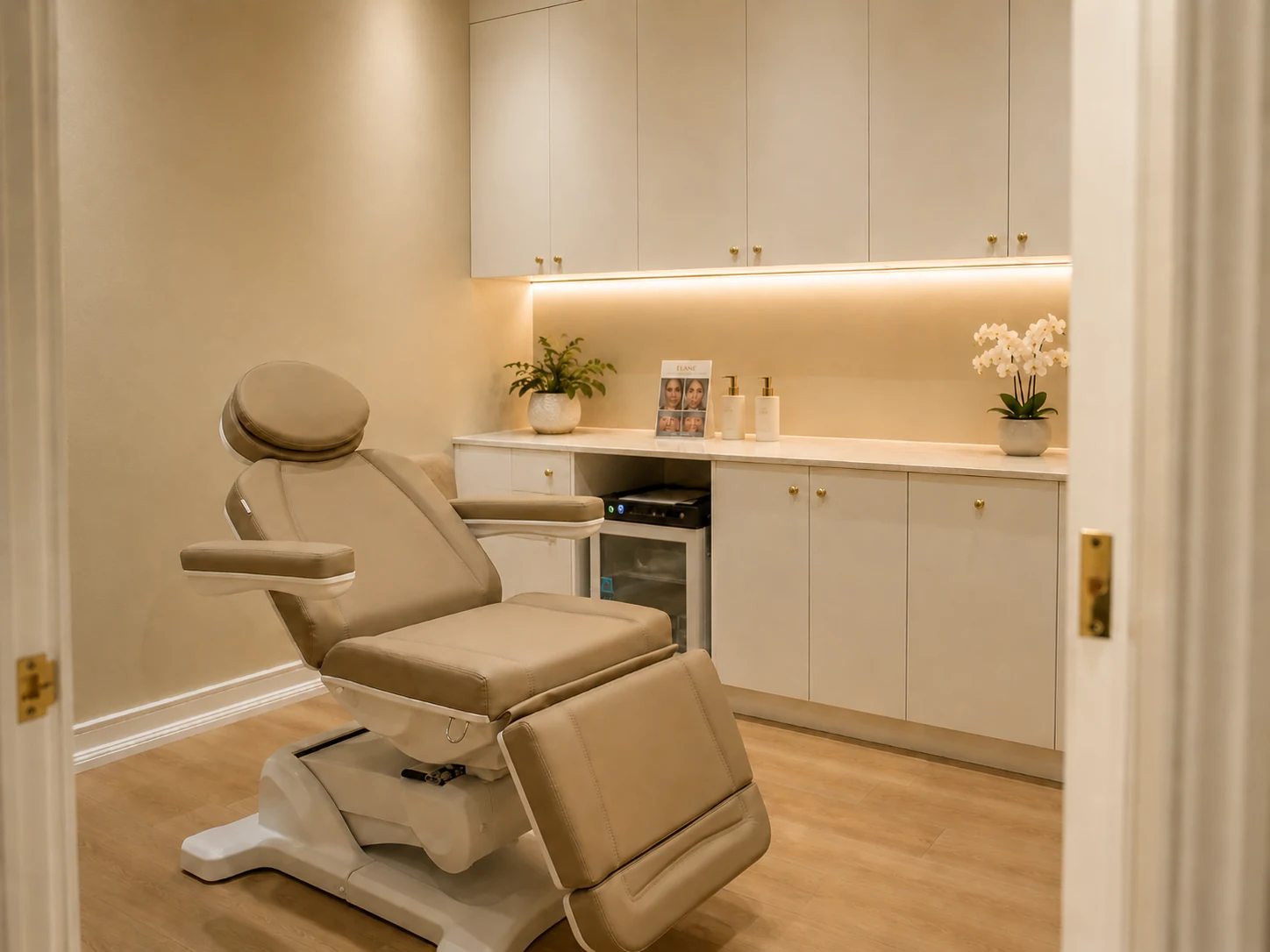 An Élané Aesthetics treatment room — reclining treatment chair, warmly lit cabinetry and fresh orchids